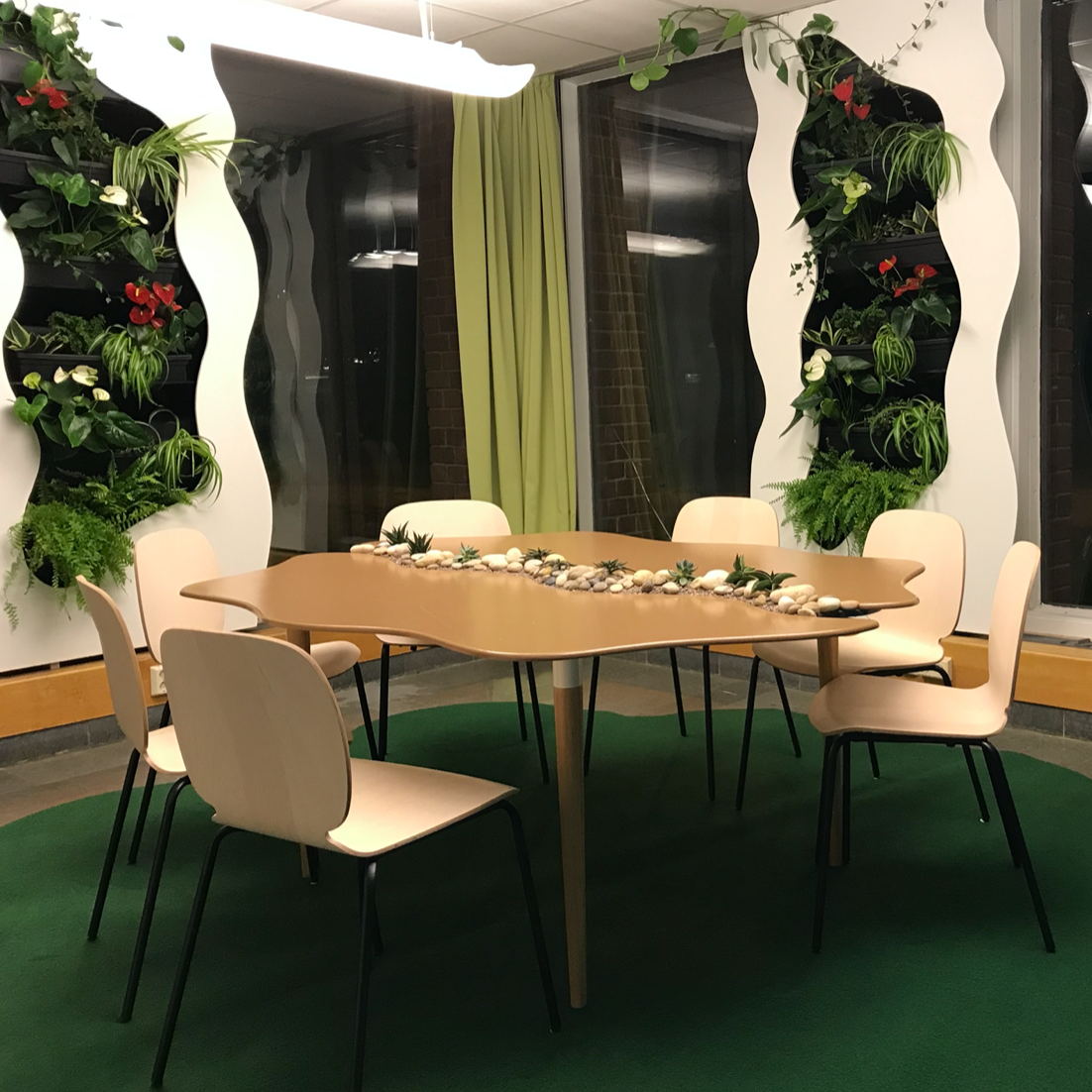 A conference room with a round and wave-shaped table as well as wave-shaped panels between the windows that houses living plants.