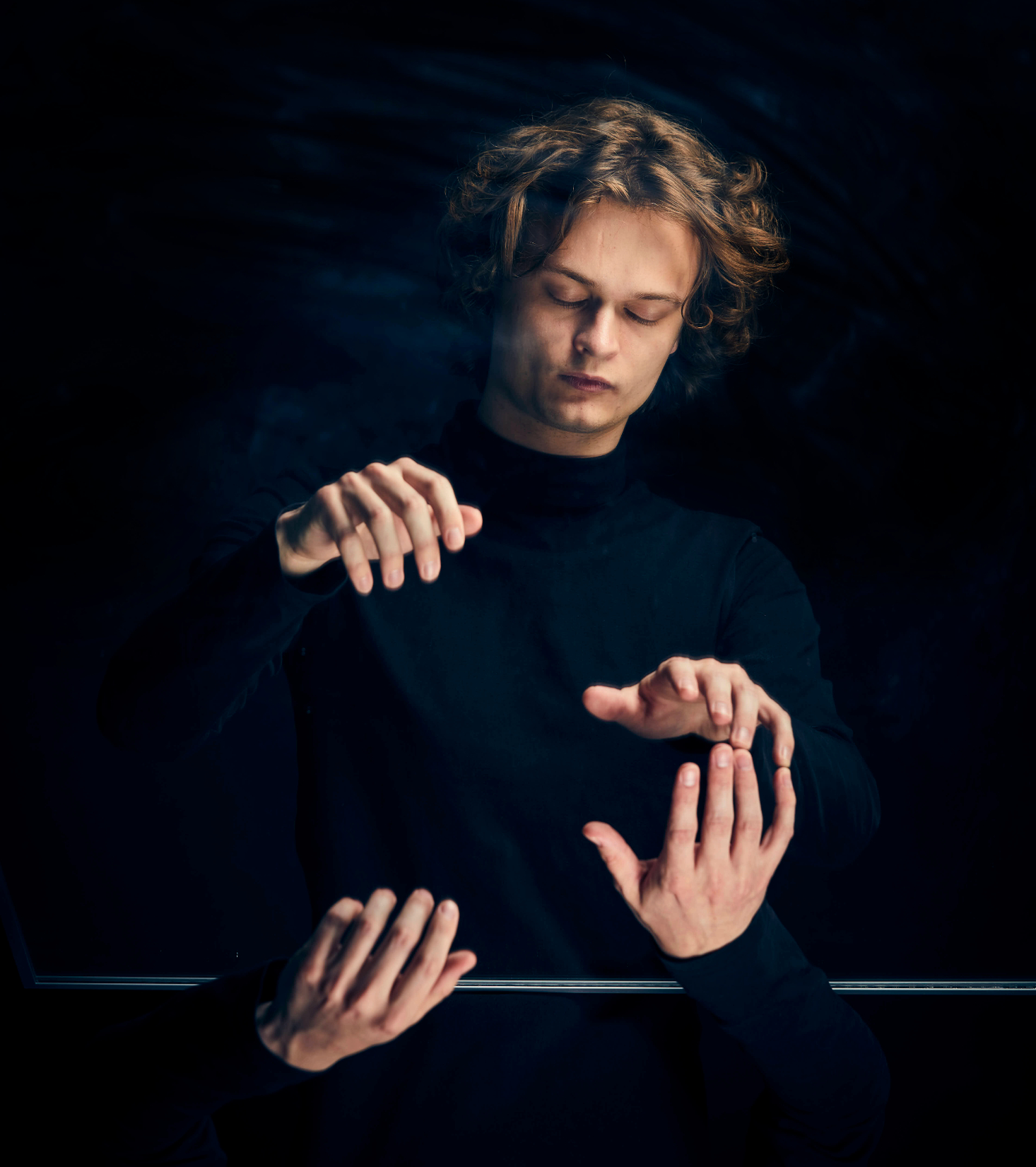 Surrealistiskt foto på Gustav Piekut. Han blundar, händerna ser ut att spela piano i luften. Händerna i spegelvänd form sticker upp i fotots nederdel. Fingertopparna på Gustavs ena hand snuddar spegelhandens fingertoppar.