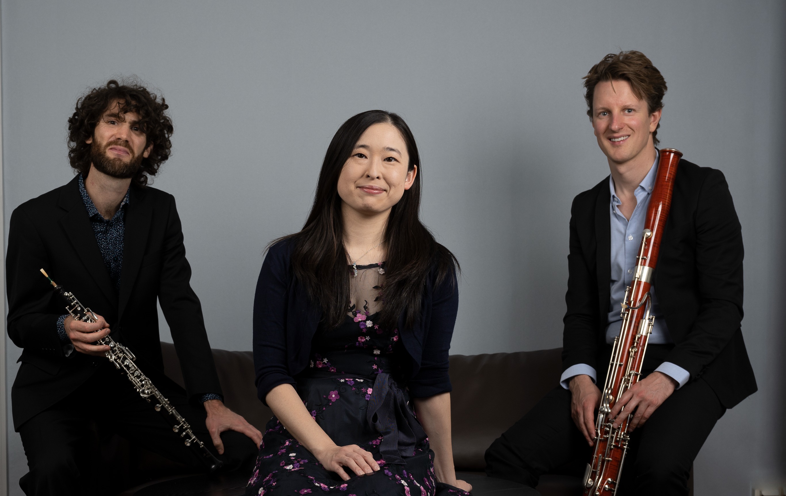 Musikerna i Trio Nastela sitter leende på rad. Emmanuel Laville med en oboe, Asuka Nakamura, Sebastian Stevensson med en fagott.